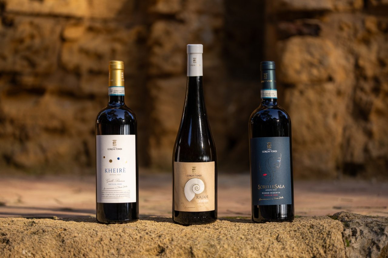 Three Tenuta Gorghi Tondi bottles, Kheir&egrave;, Raj&agrave;h and SorelleSala, standing on a sunlit stone ledge.