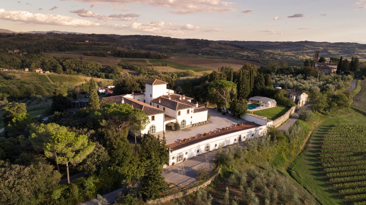 Aerial view of Fattoria San Michele a Torri, a white villa and farm buildings among trees, olive groves and vineyards.
