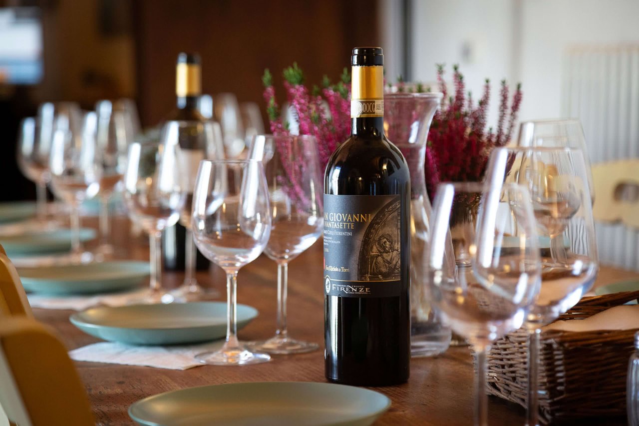 A long table laid with wine glasses and a bottle of San Giovanni '97 for a tasting at Fattoria San Michele a Torri.