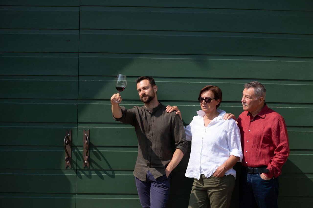 Three members of the Brunelli family against a green wall, one raising a glass of red wine