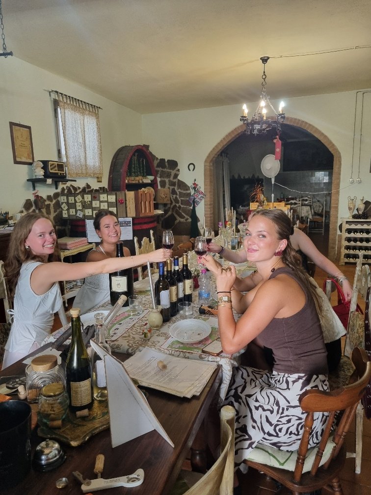 Three guests raising glasses of red wine at the tasting table at Pasqualetti Viticoltori with the brick arch of the tasting room behind