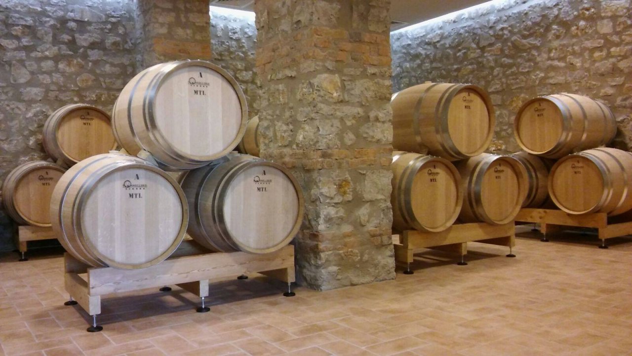 Oak barrels on wooden racks between stone walls and pillars in the La Carraia barrel cellar