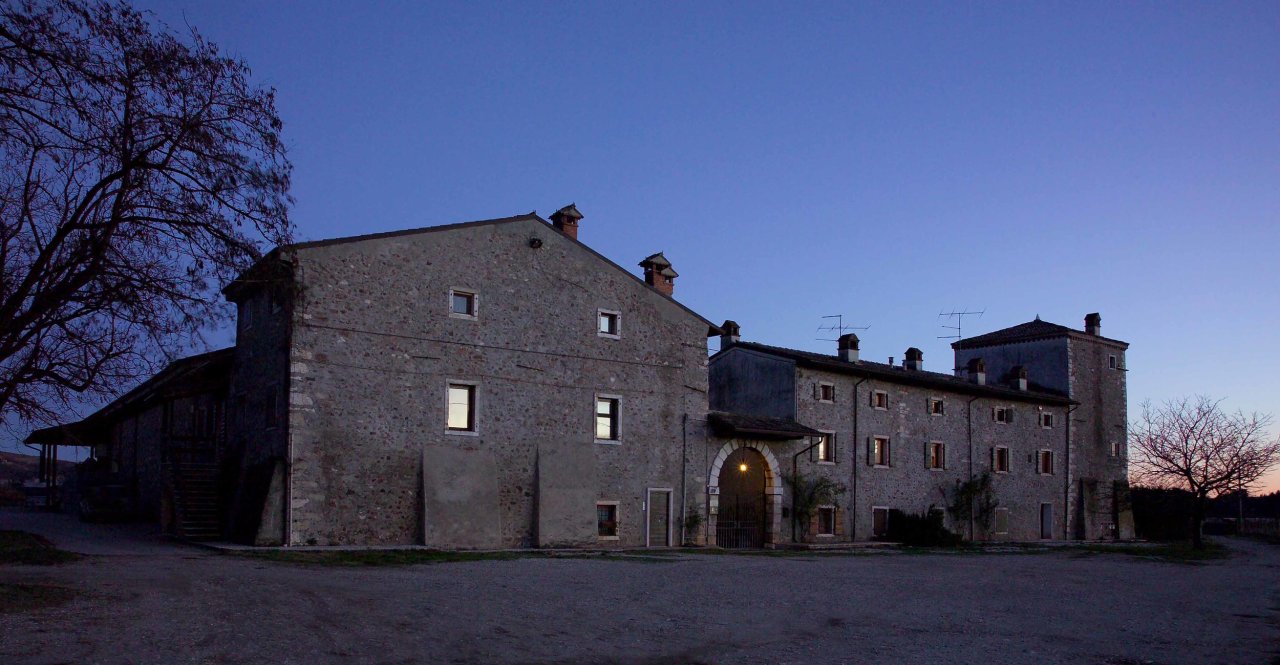 The farmhouse of Le Fraghe at dusk, with the lit entrance arch and the tower