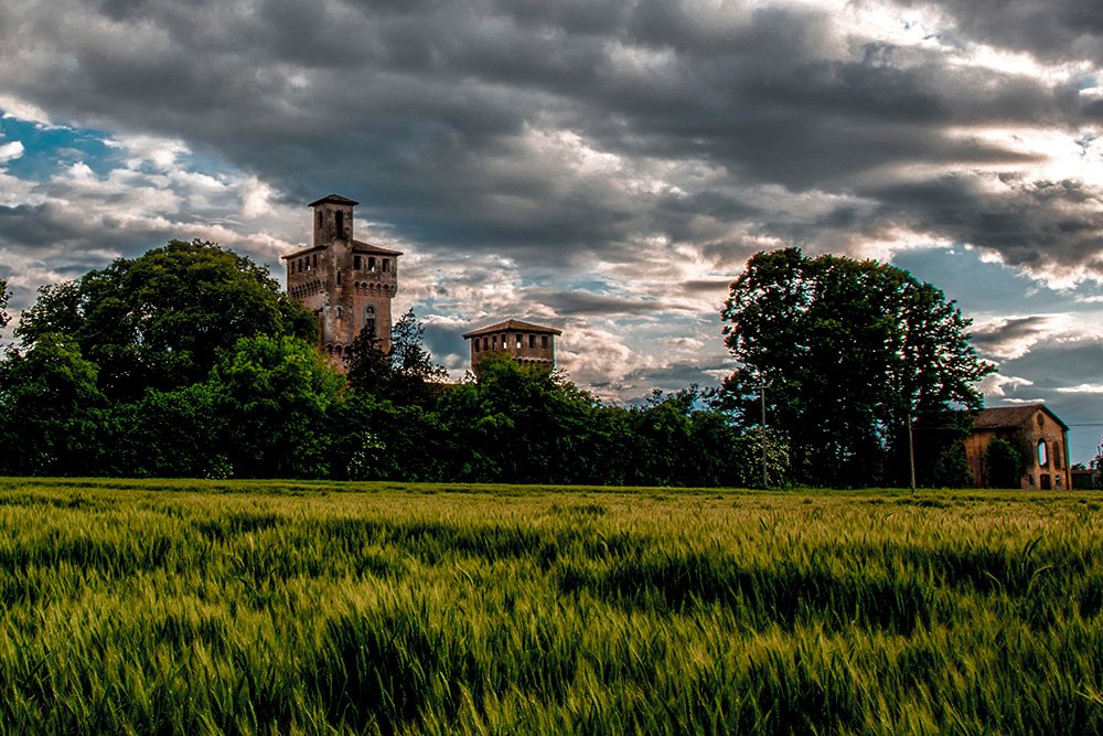 The castle of Villa Oppi seen across a green field under a cloudy sky
