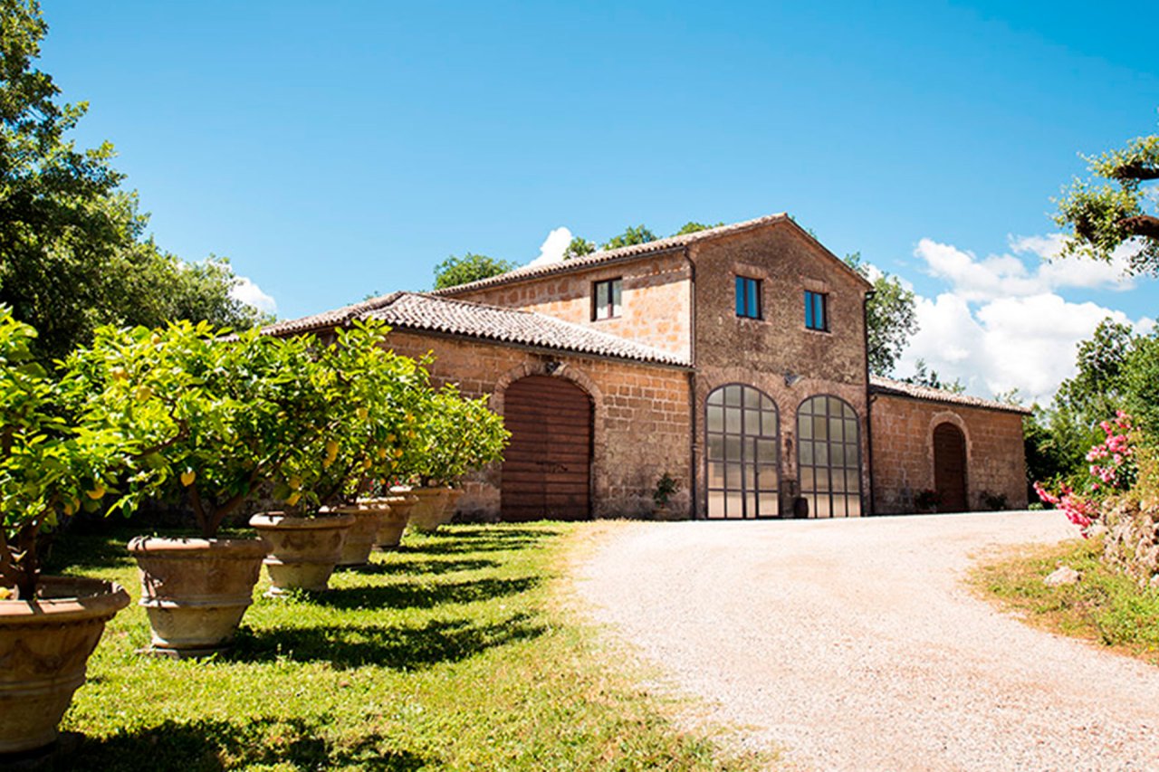 Brick and stone farmhouse with arched glass doors and potted lemon trees along the drive at Cantine Neri