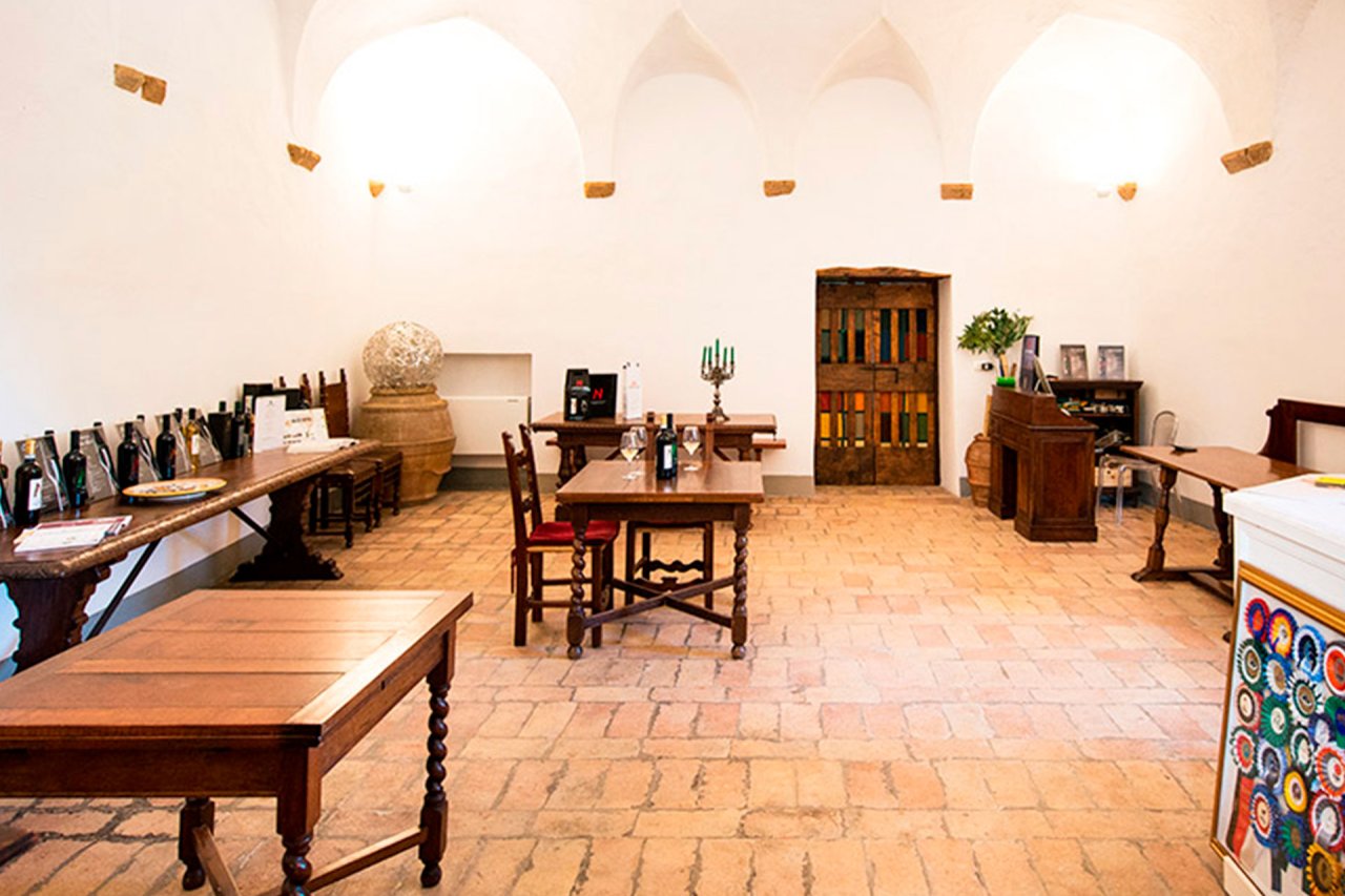 Tasting room with a vaulted white ceiling, terracotta floor and wooden tables at Cantine Neri