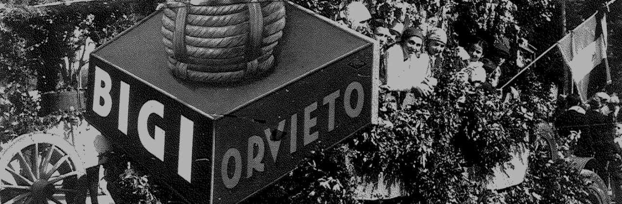 Black and white archive photo of a giant Bigi Orvieto box with a straw-wrapped flask on top, people and a flag behind