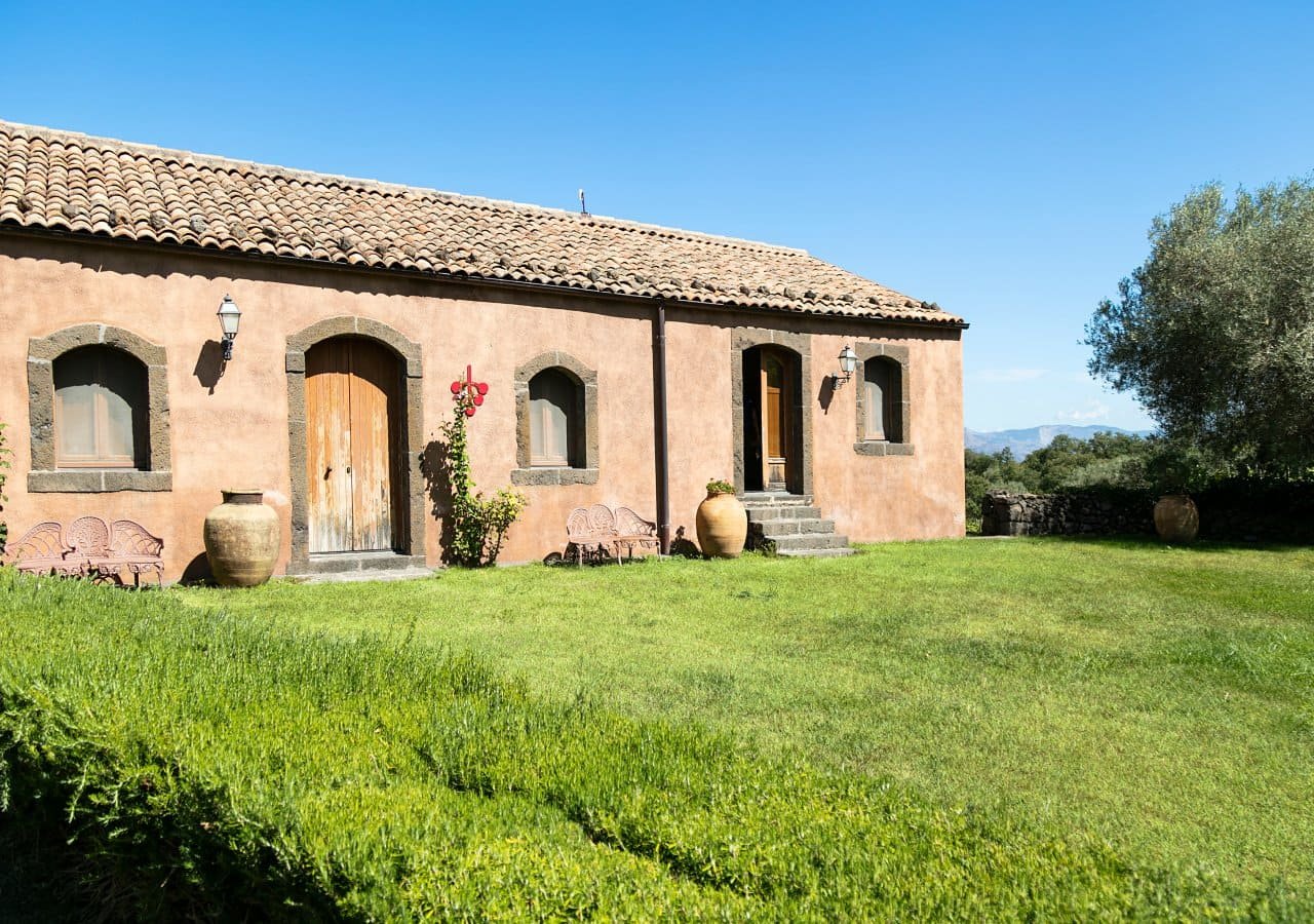 Stone farmhouse with arched doorways and a lawn at Terrazze dell'Etna