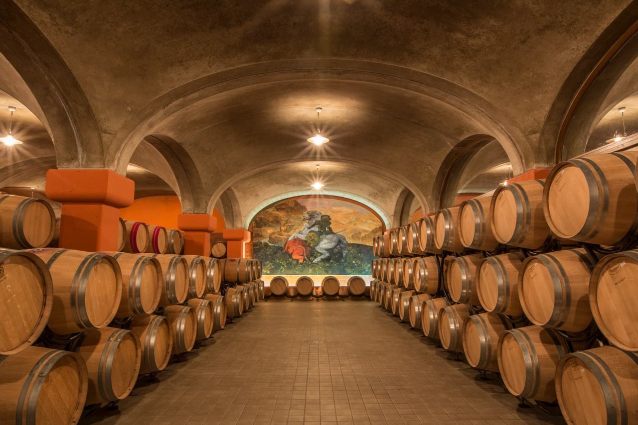 Tua Rita's barrel cellar, rows of barrels under a vaulted ceiling with a painted end wall
