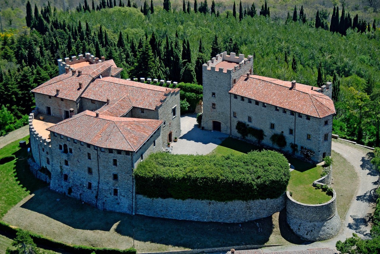 Aerial view of Castello di Montegiove, with its stone walls, crenellated tower and round corner bastion among the woods