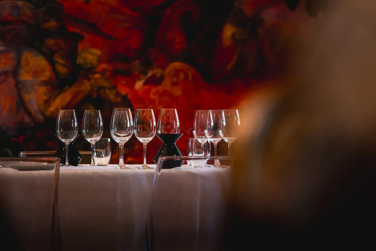 Wine glasses set on a white tablecloth in front of the painted wall of Tua Rita's cellar