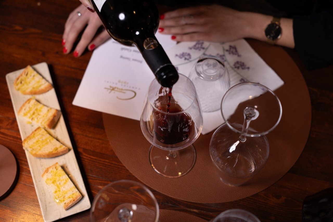 Red wine being poured at a Guidi 1929 tasting, with bread and tasting sheets on the wooden table