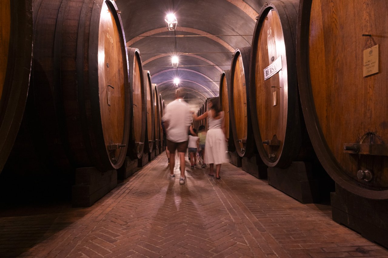 Visitors walking between the large oak casks in Bersano's historic cellar at Nizza Monferrato