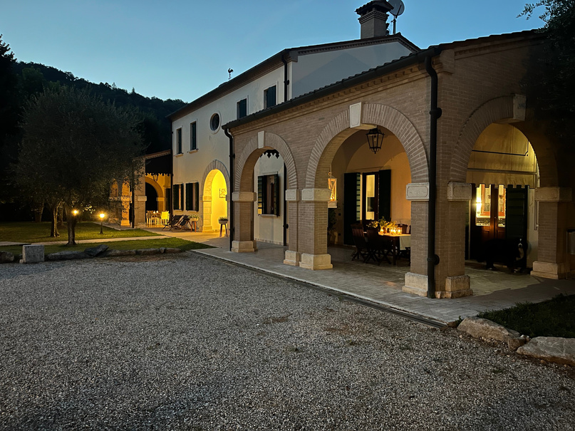 The brick house of Ca&rsquo; Avignone at dusk, its arched porch lit and the gravel yard in front