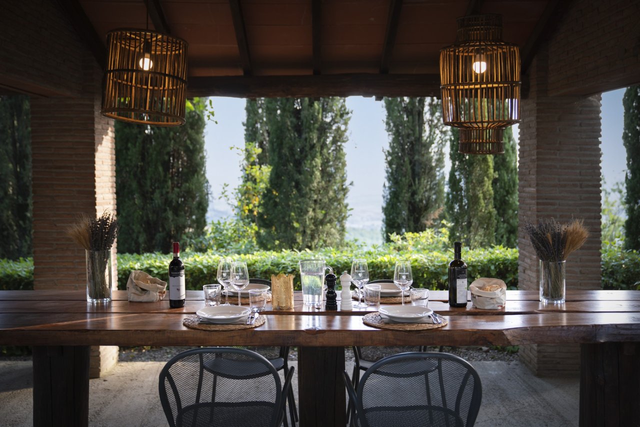 Long wooden table laid with glasses and wine bottles under a brick loggia at Buccia Nera