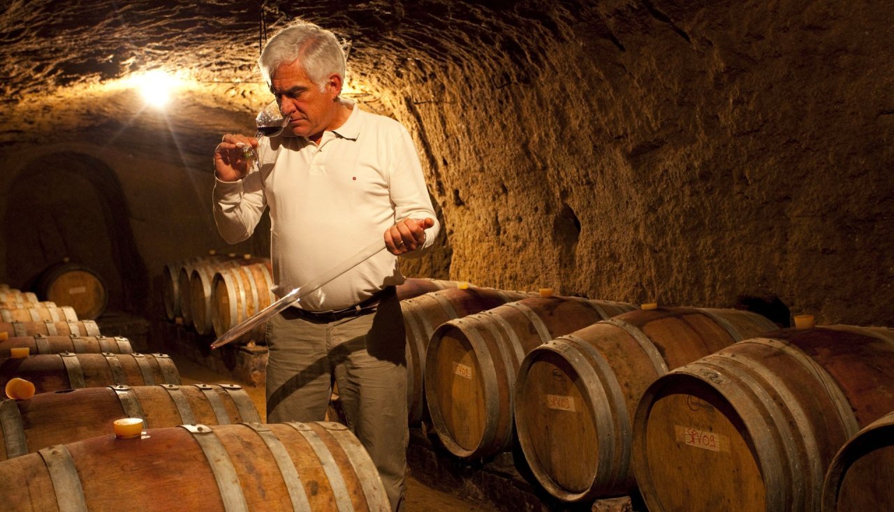 A man smells a glass of wine among the barrels in the tuff cellar at Tenuta Le Velette