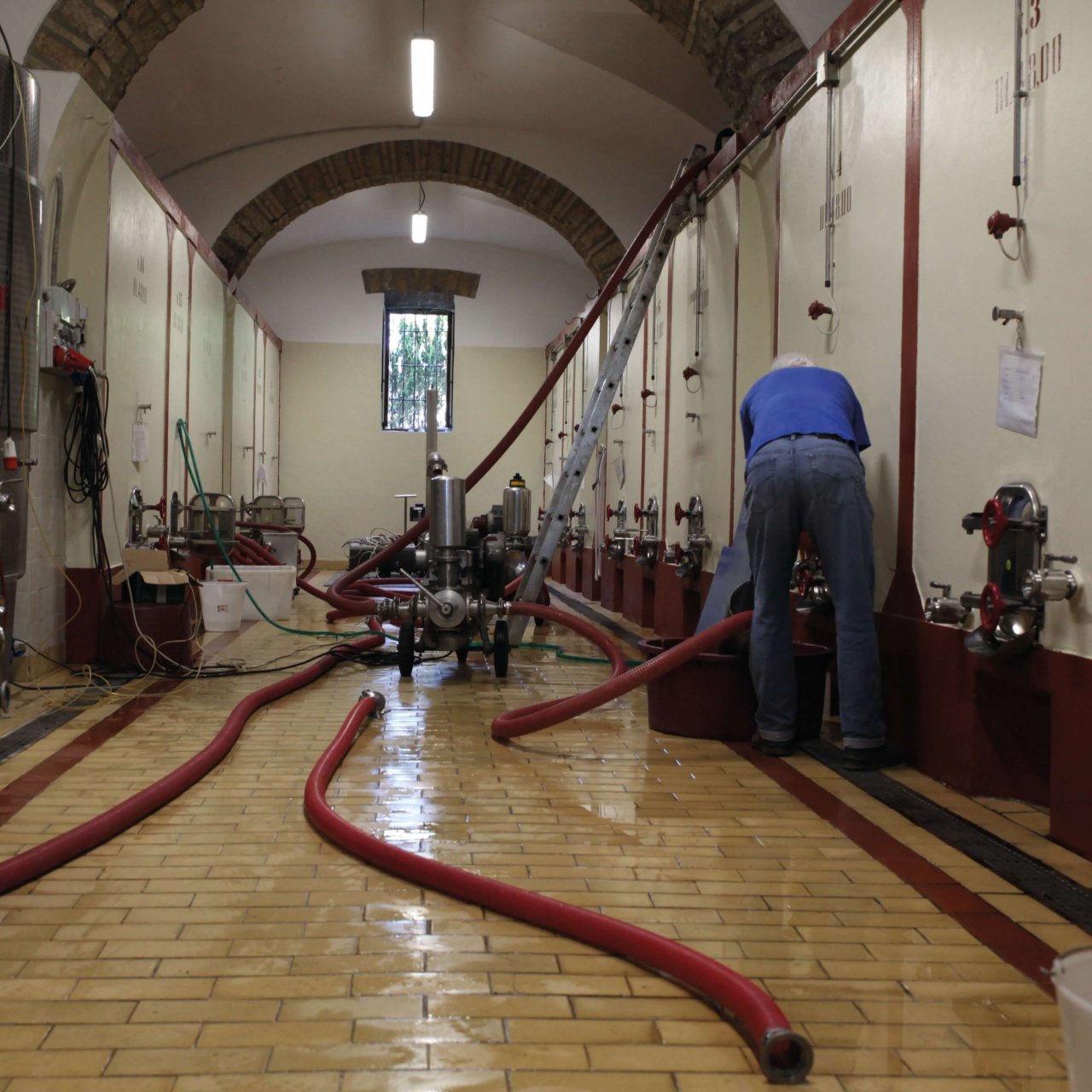 A worker at the tanks in the vaulted cellar at Tenuta Le Velette, with hoses across the floor