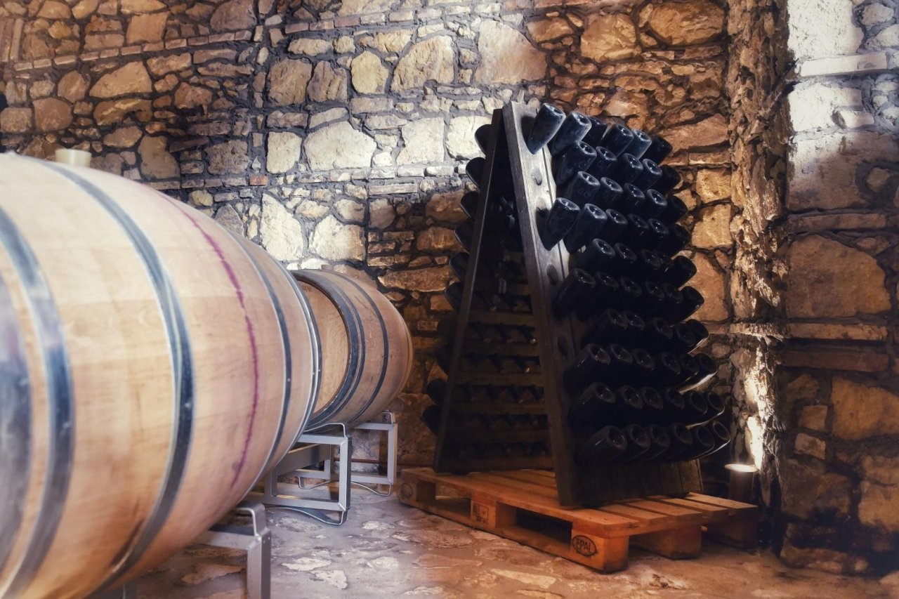 Oak barrels beside a wooden rack of bottles resting neck-down in a stone-walled cellar at Casa Divina Provvidenza