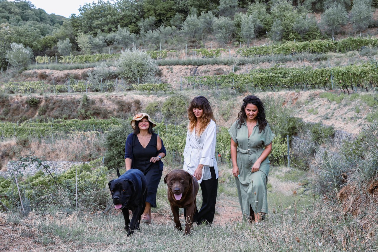 Three women with two Labradors standing between the terraced vines at Tenuta del Travale