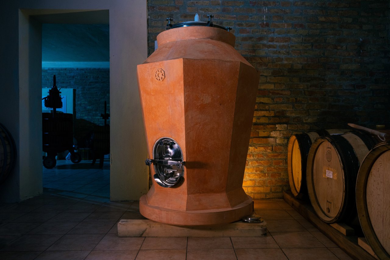 A cocciopesto amphora on its stand in the cellar at Tenuta del Travale, with barrels behind it