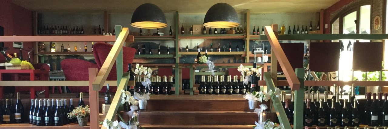 The wine shop at Tenuta del Buonamico with shelves and steps lined with bottles under two large pendant lamps
