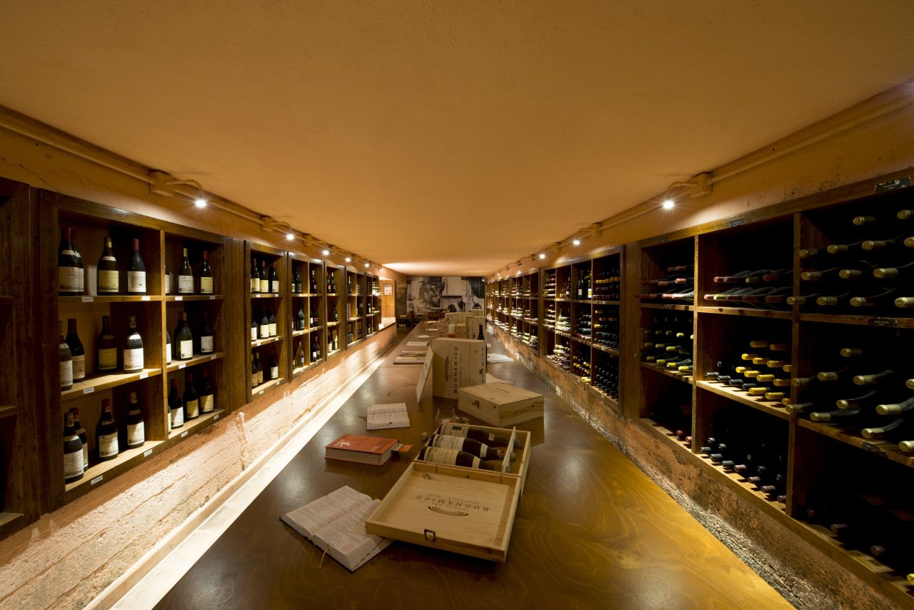The historic cellar at Tenuta del Buonamico, a long room of wooden shelves holding old bottles, with wine boxes on a central table