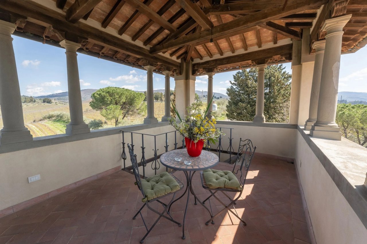 Covered loggia with stone columns and a small table and chairs, looking out over vineyards at Corte di Valle