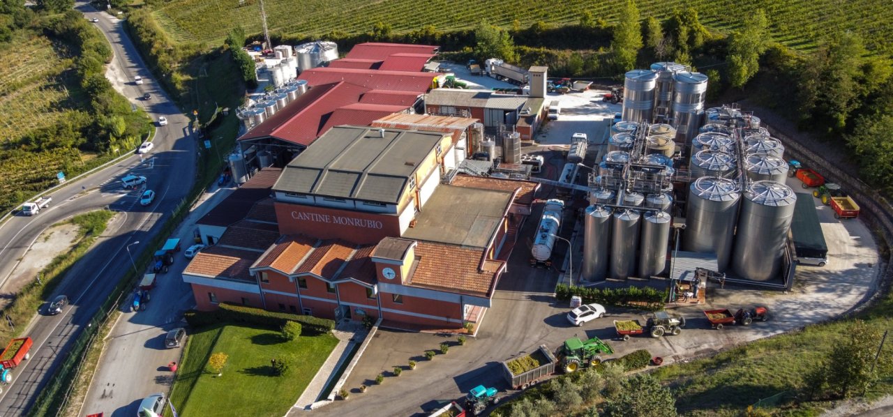 Aerial view of the Cantine Monrubio cellar, with rows of steel tanks and tractors pulling grape trailers