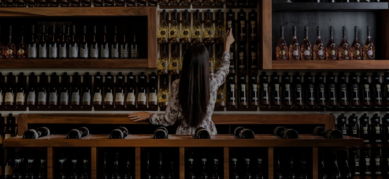 A woman reaching for a bottle on the floor-to-ceiling wine wall in the 47 Anno Domini shop at Roncade