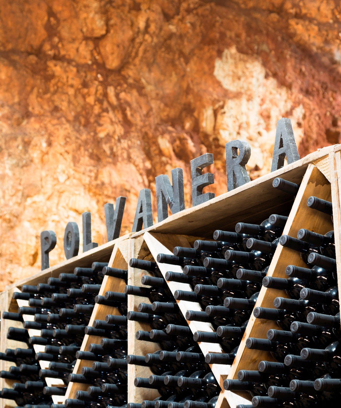 Bottles racked in wooden bins under the Polvanera name, against the red rock wall of the cellar
