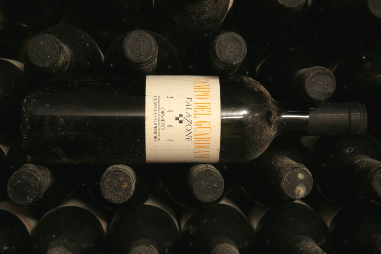 A dusty bottle of Palazzone Campo del Guardiano lying on stacked older bottles in the cellar
