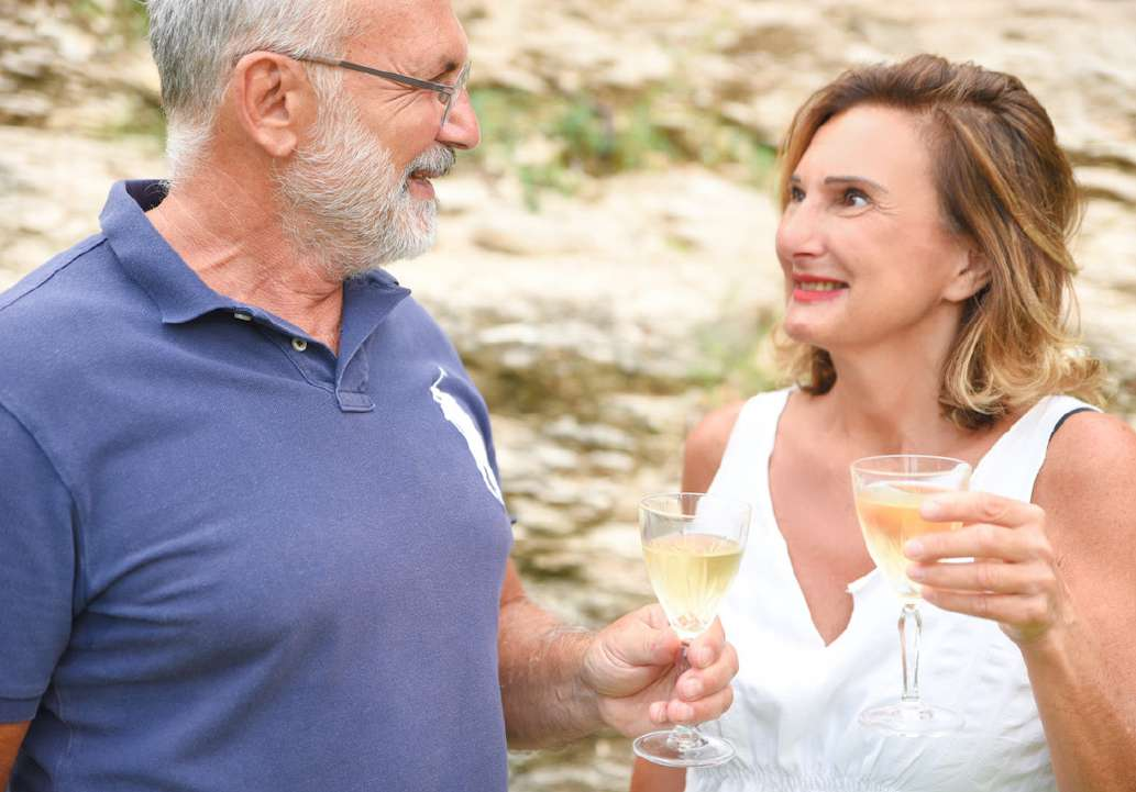Nicola Ercolino and Antonella La Sala of Ca&rsquo; Avignone raising glasses of white wine by a stone wall