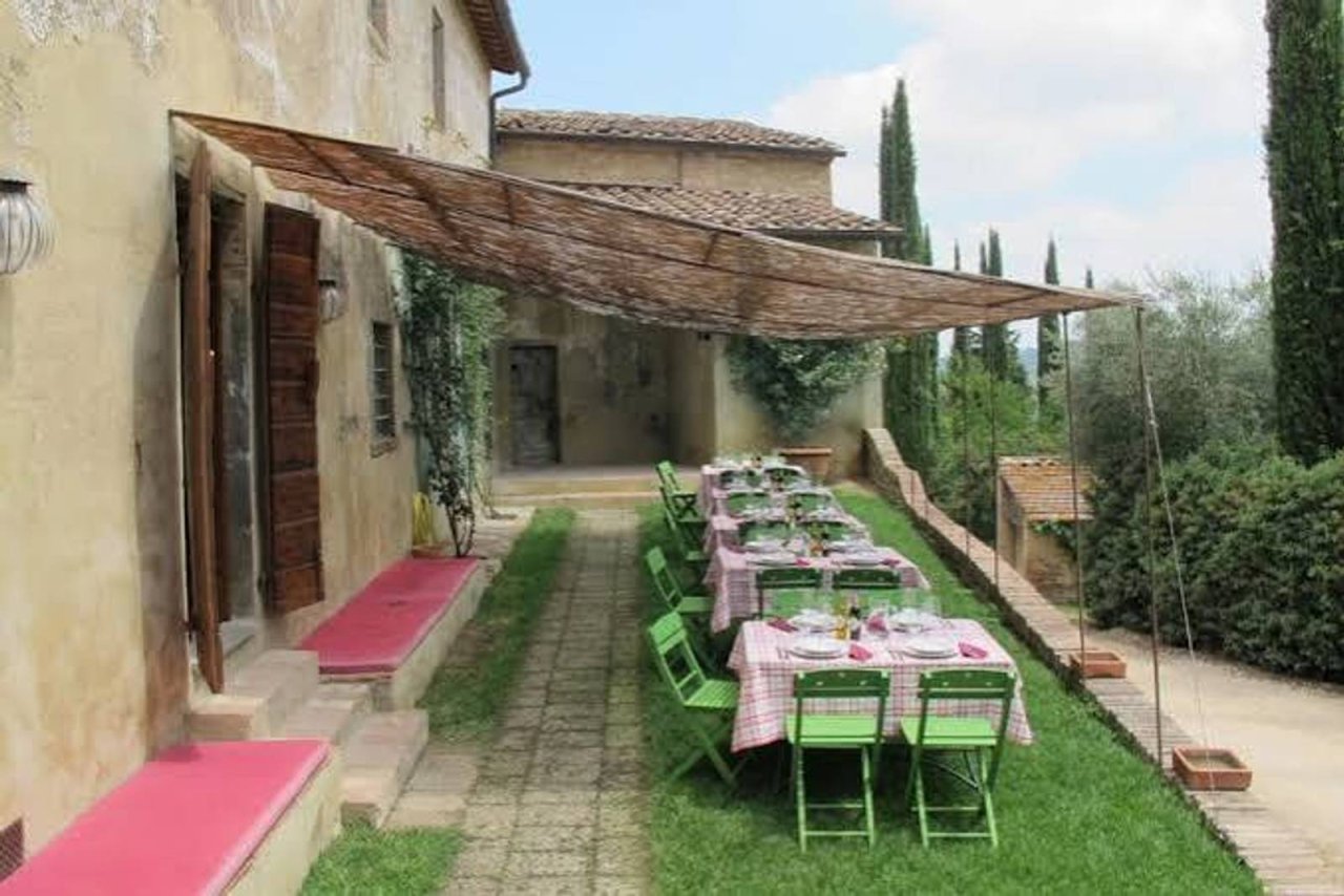 Tables set under a shade canopy in the garden of the Castello Sonnino Enoteca, with cypresses beyond