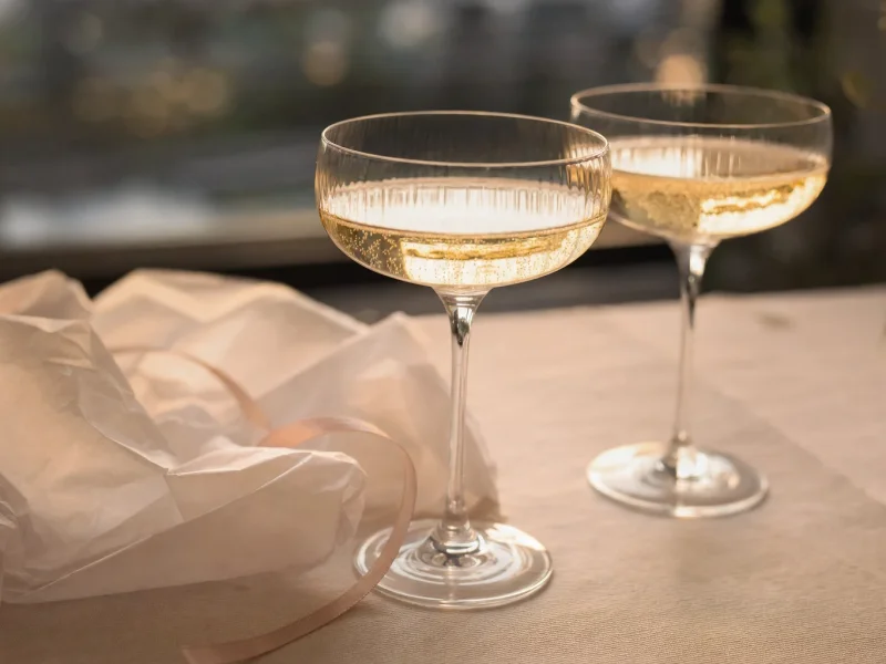 Two glasses of pale sparkling wine beside tissue paper and ribbon