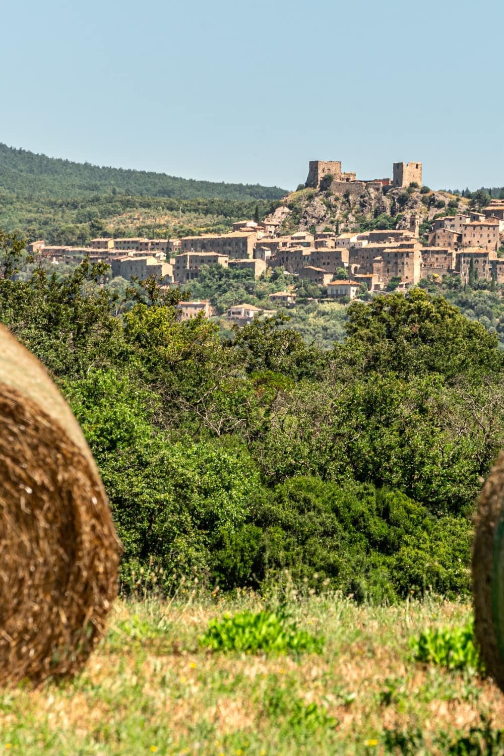 The hill village of Montemassi seen across a field with a hay bale from Rocca di Montemassi