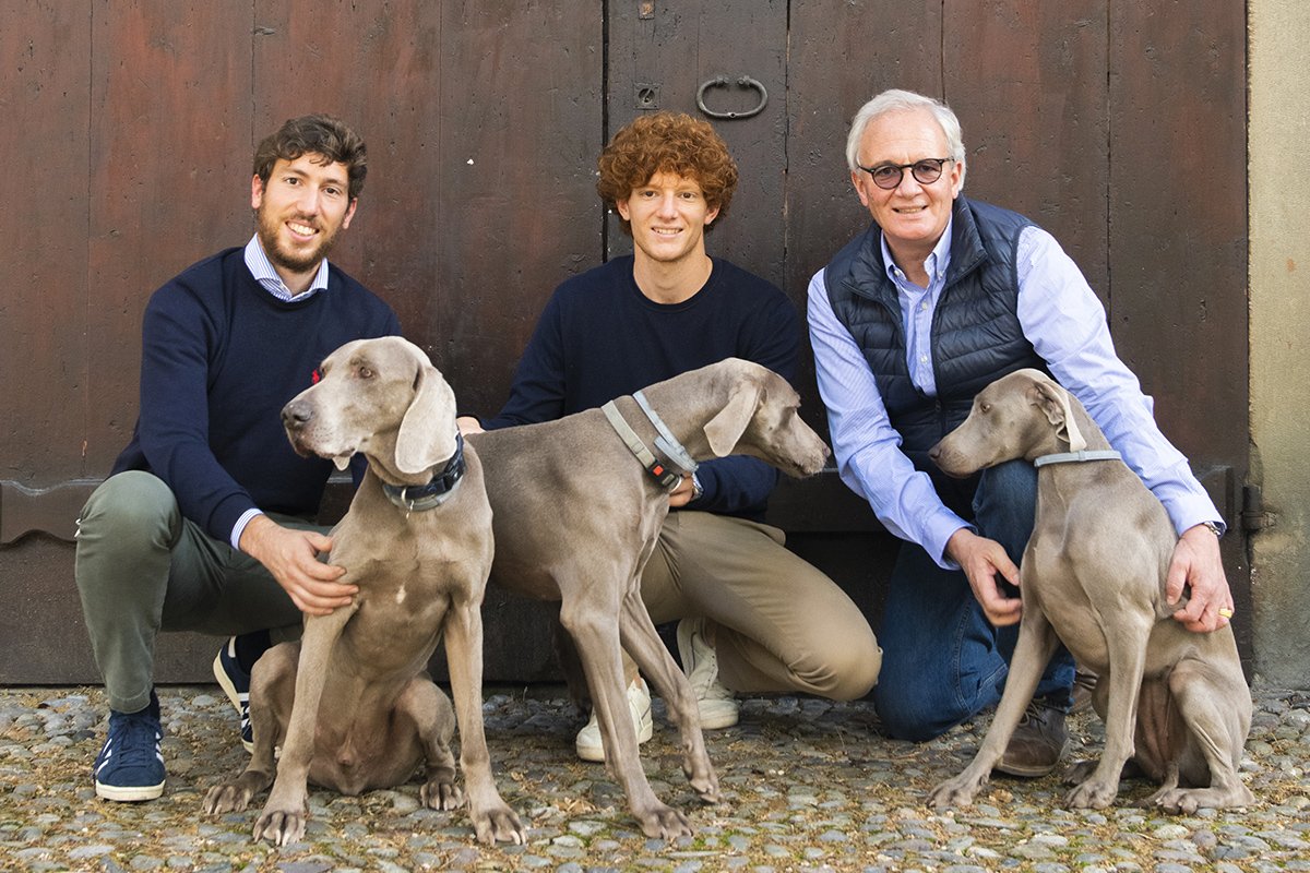 Gualberto, Filippo and Riccardo Ricci Curbastro crouching with their three Weimaraner dogs in front of a wooden door