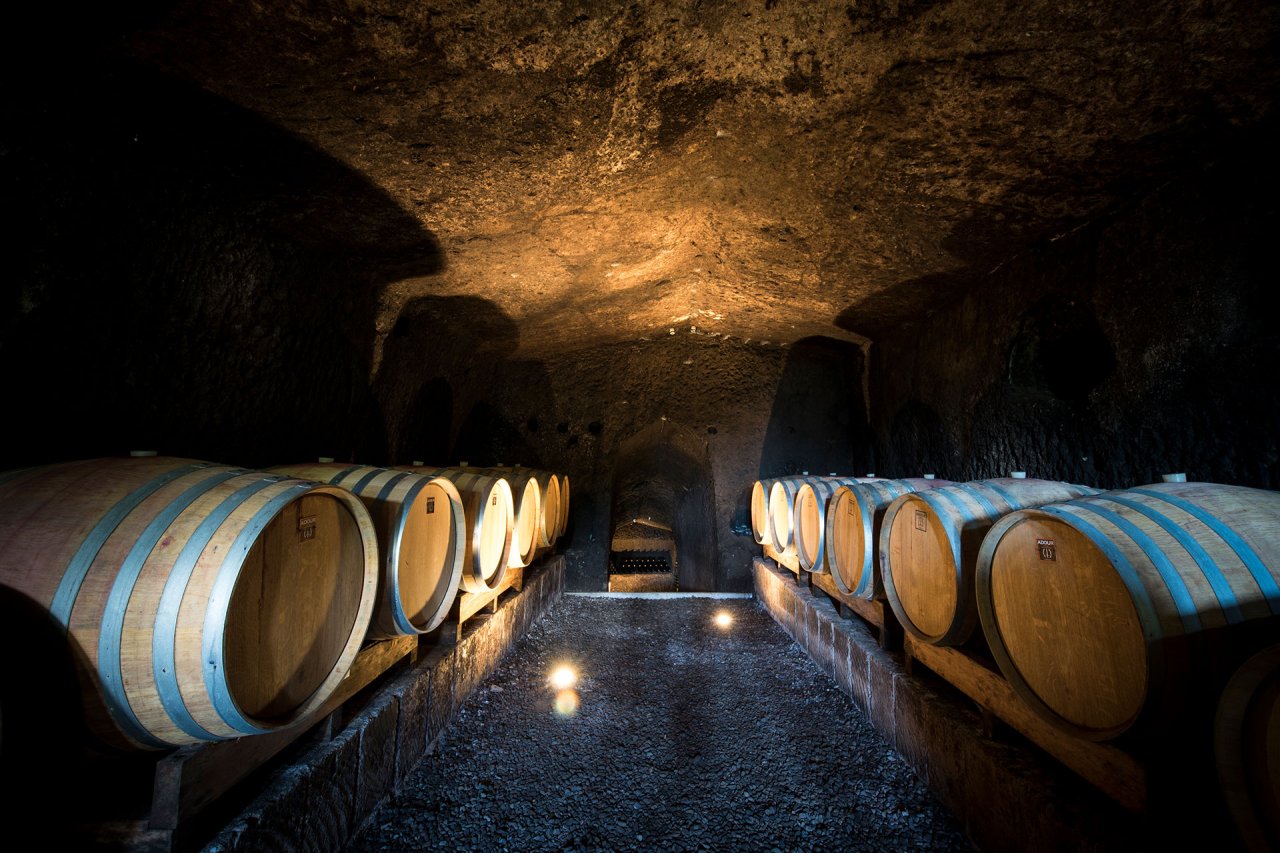 Oak barrels in rows on both sides of a lit path in the cave cellar at Cantine Neri