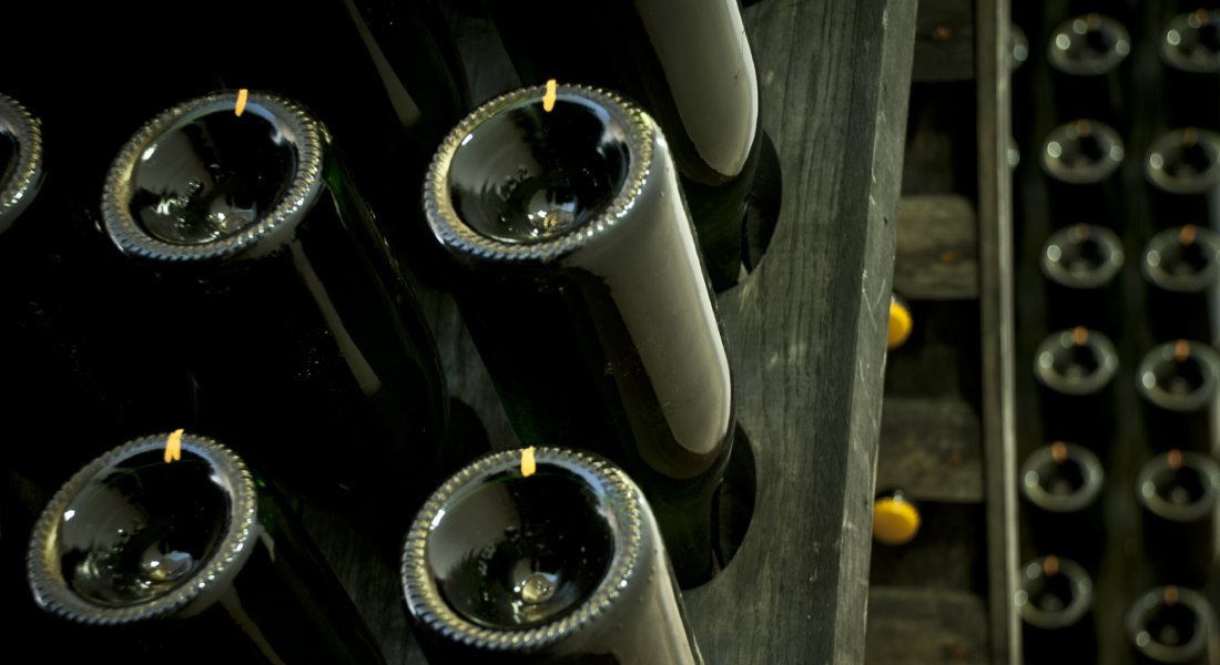 Sparkling wine bottles resting neck-down in wooden riddling racks in the Terrazze dell'Etna cellar