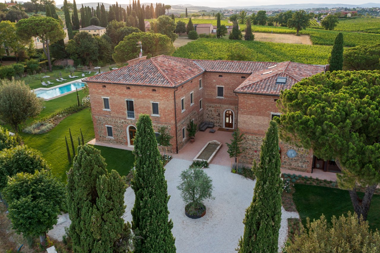 The brick villa at Fattoria Svetoni seen from above, with its pool, gardens and cypress trees
