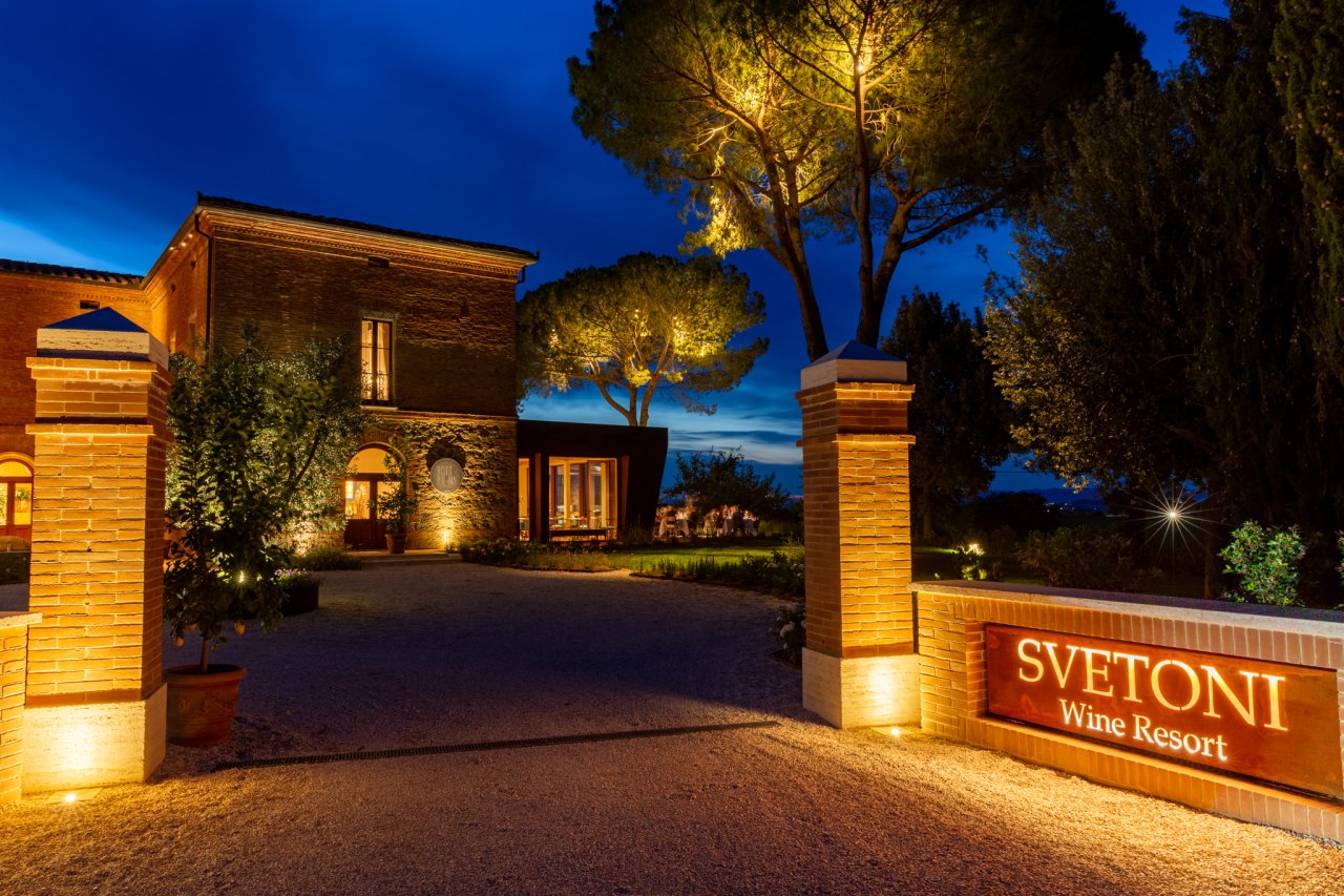 The lit entrance of Fattoria Svetoni at dusk, with the Svetoni Wine Resort sign and the villa behind