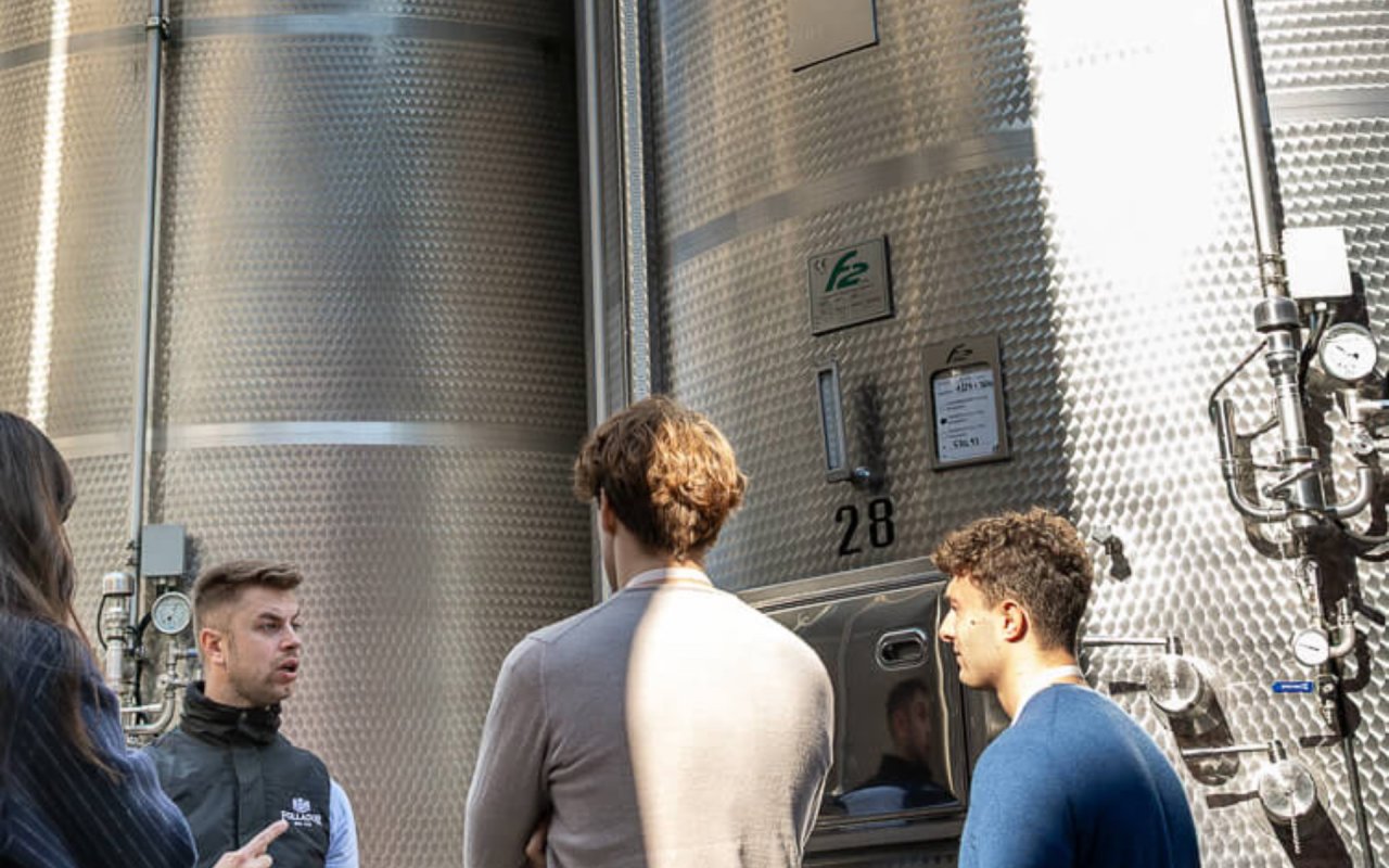 A guide in a Follador gilet explaining the steel tanks to visitors on a cellar tour