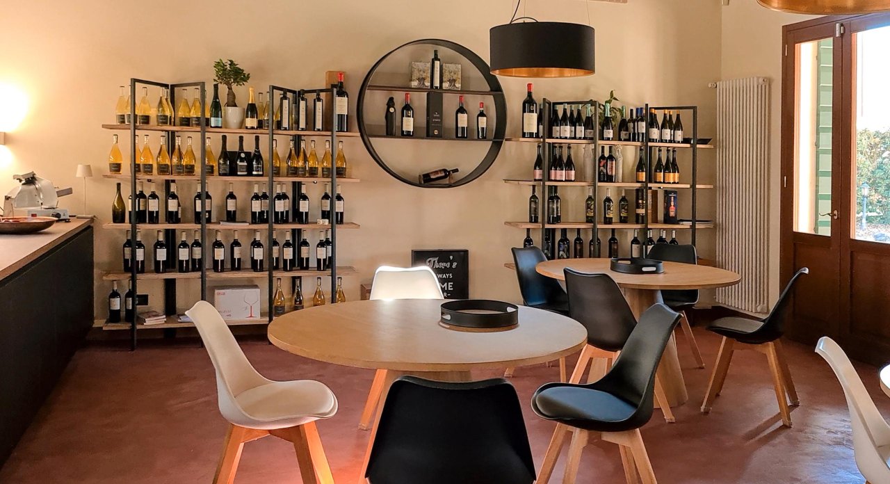The tasting room of Ca&rsquo; Avignone, with round tables laid for a tasting and shelves of bottles
