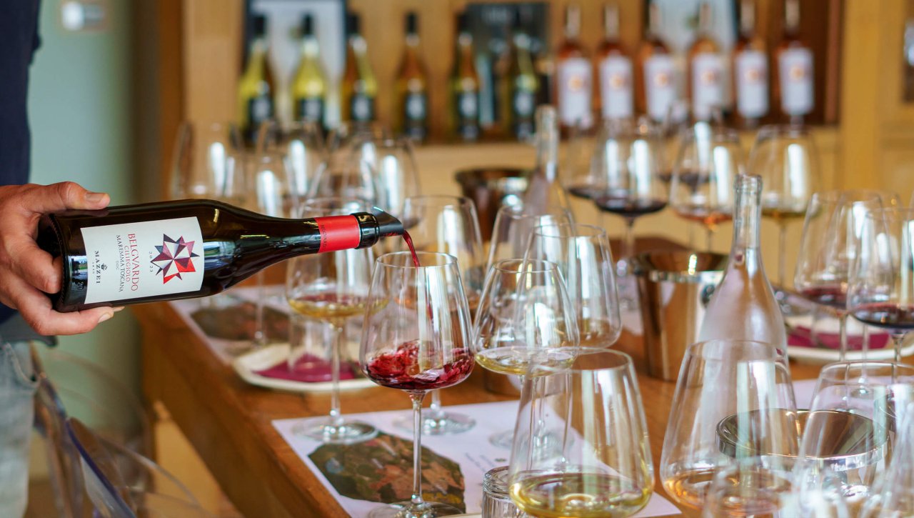 A bottle of Belguardo poured at a tasting table lined with glasses in the estate's tasting room