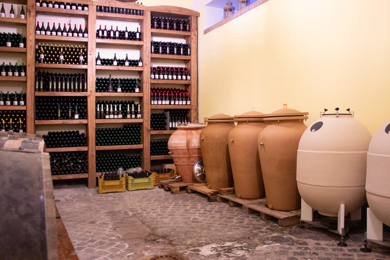 Clay amphorae and egg-shaped jars beside shelves of bottles in the Cantine degli Astroni cellar