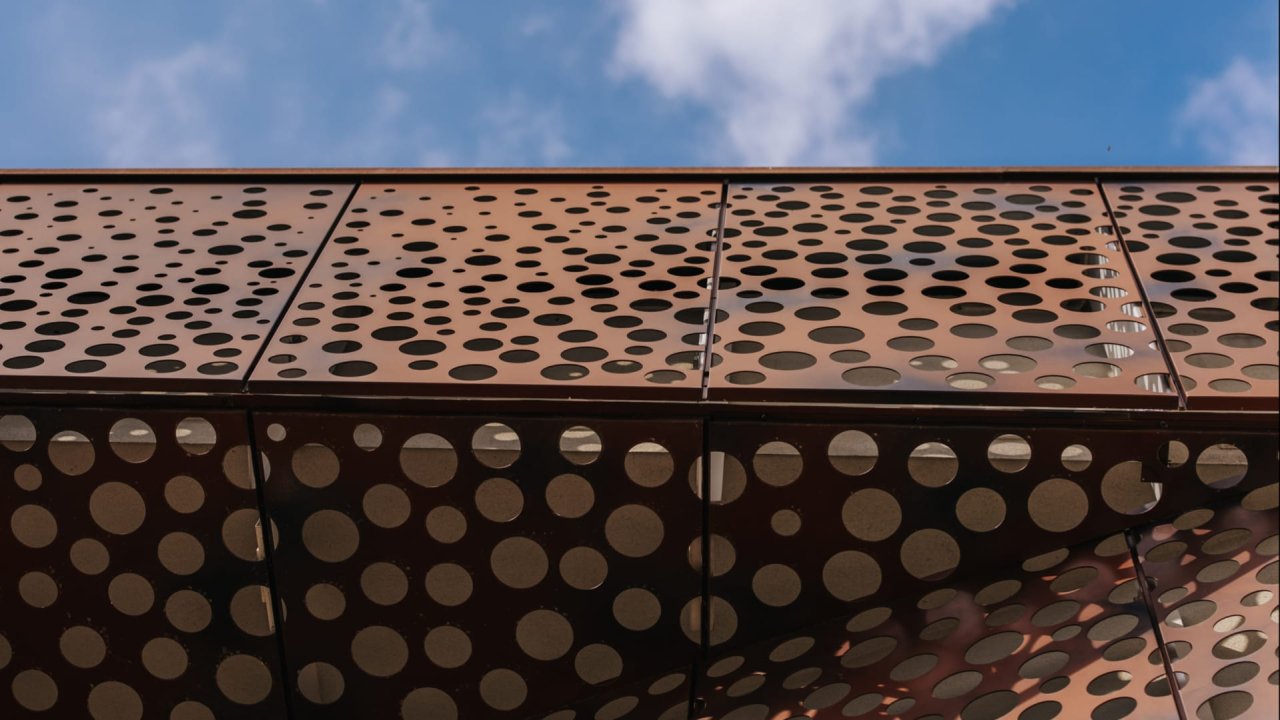 The perforated rust-coloured metal facade of the Val d'Oca Wine Center against a blue sky