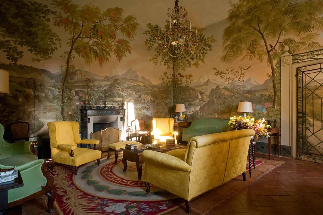 A sitting room at Castello Sonnino with painted landscape walls, yellow armchairs and a fireplace