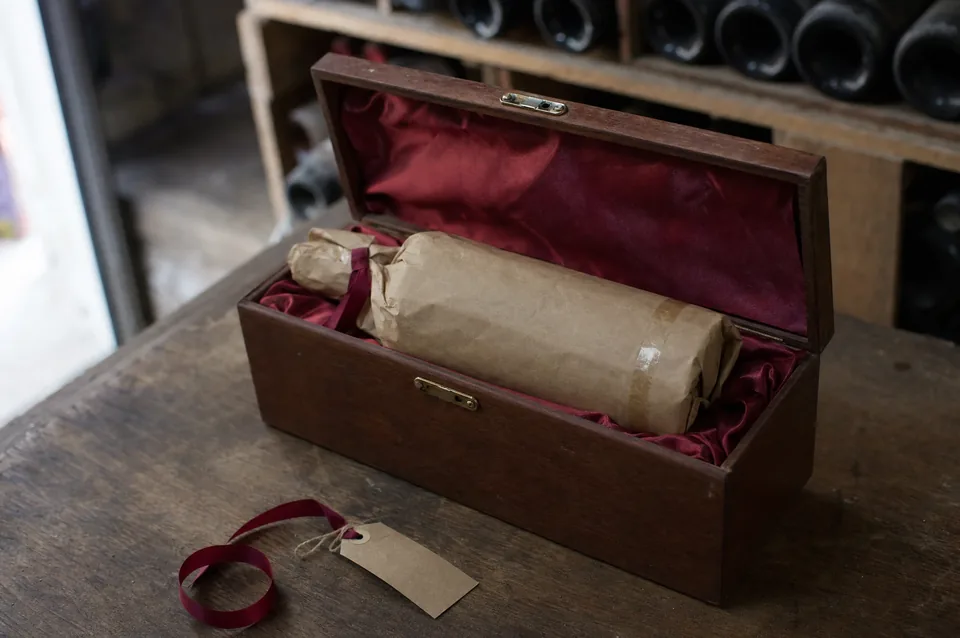 A wine bottle wrapped in paper and ribbon inside a silk-lined wooden gift box in a cellar